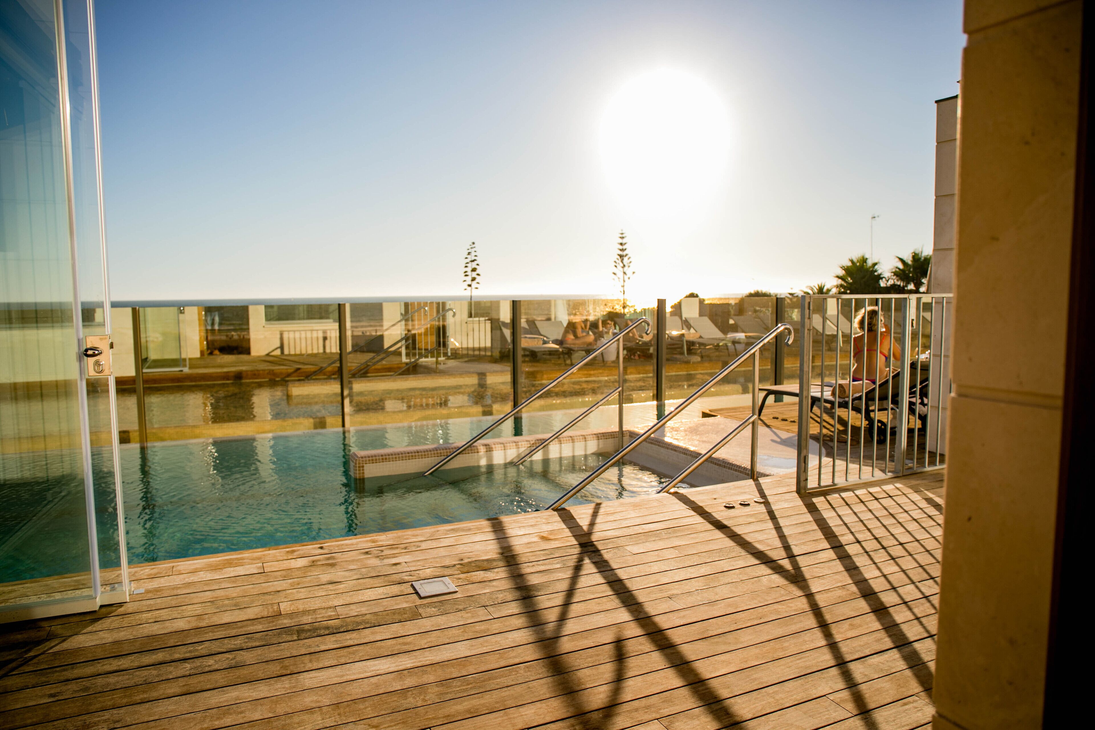 A wooden deck with a pool, glass railings, and a clear view of the pool area.