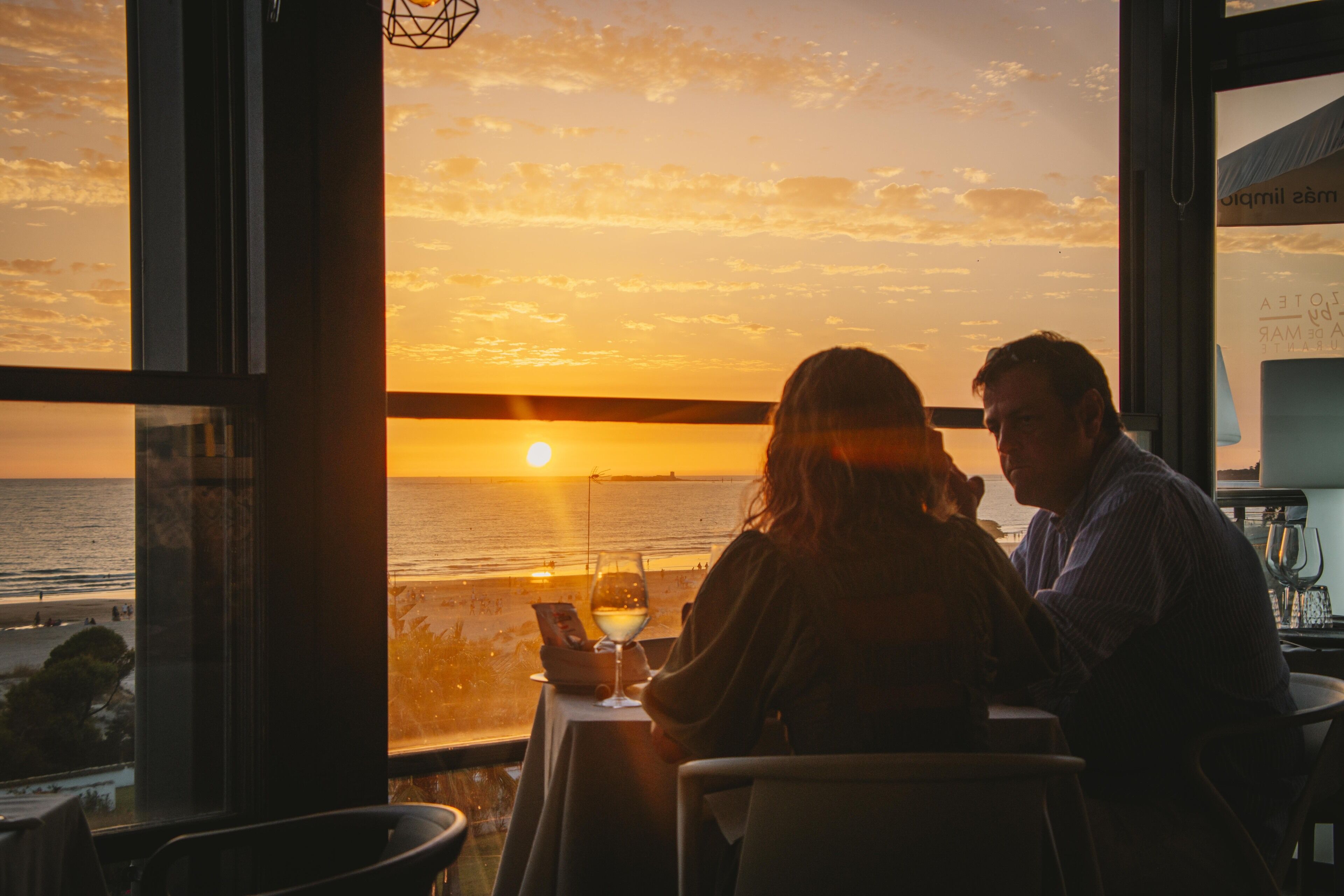 A couple dining at a table with a view of the sunset over the ocean.