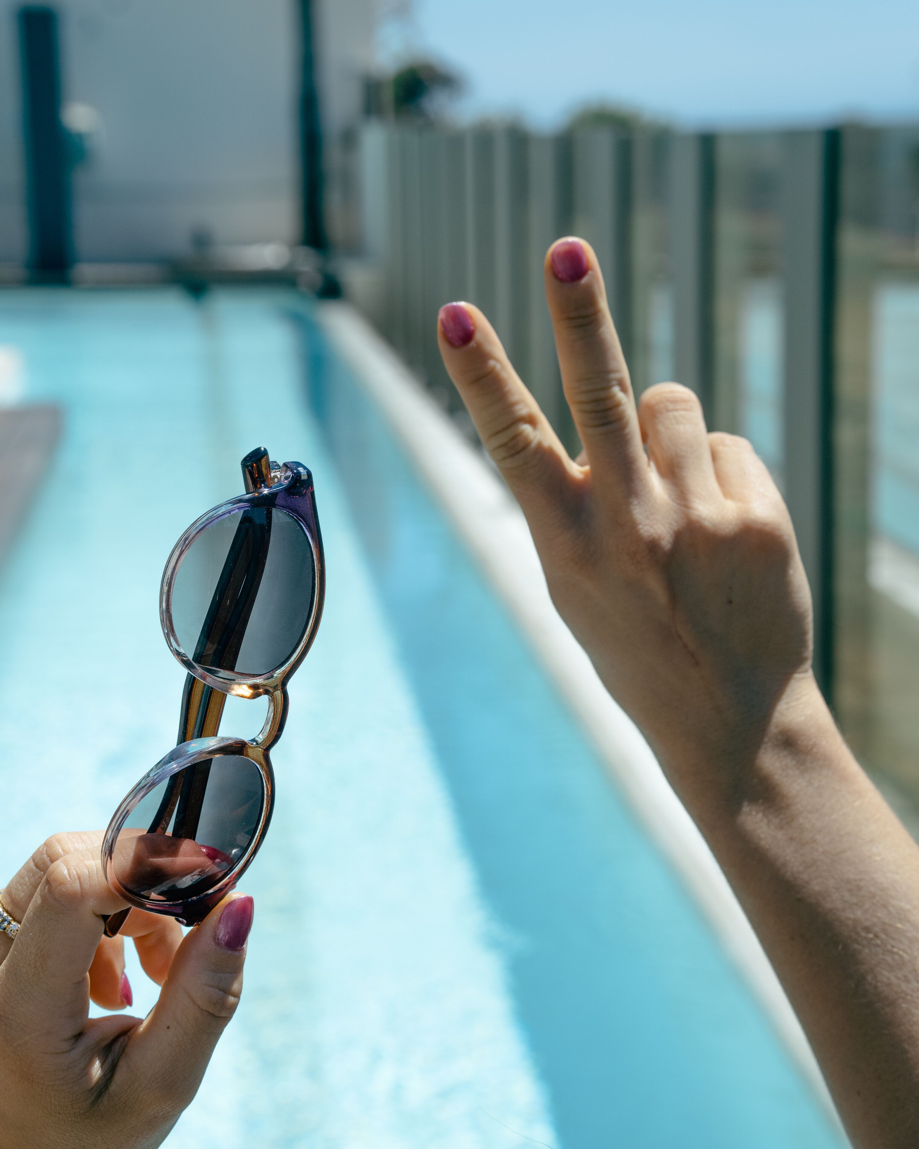 A hand holding sunglasses and making a peace sign.
