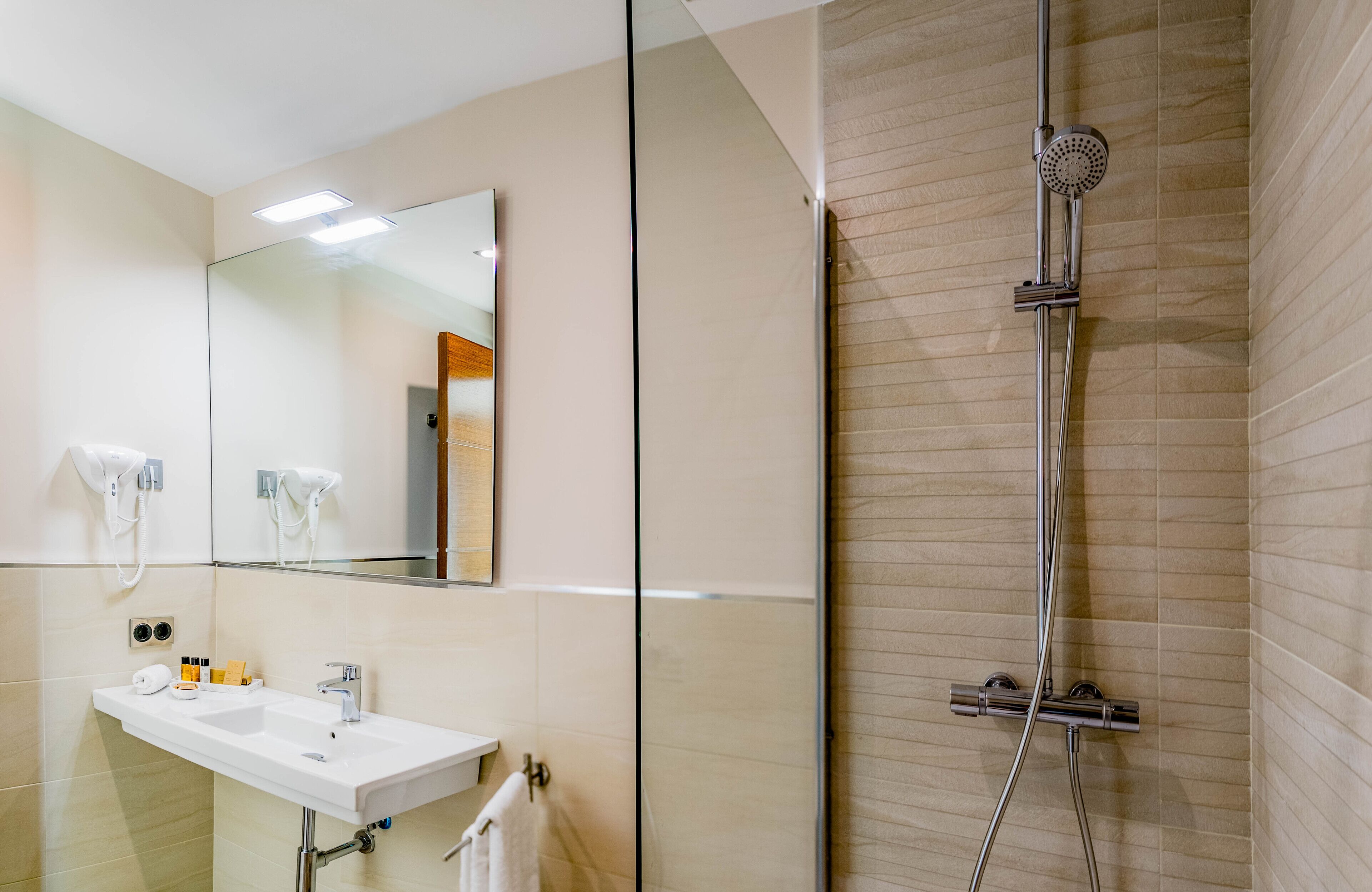 Un baño moderno con cabina de ducha de vidrio, lavamanos blanco y un espejo grande.