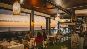 A restaurant with tables set for dining, large windows overlooking the sea, and hanging light fixtures. - Hotel Boutique Aroma de Mar (Chiclana de la Frontera)