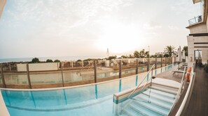 Una piscina en la azotea con vistas al mar, rodeada de sillones de descanso y sombrillas.
