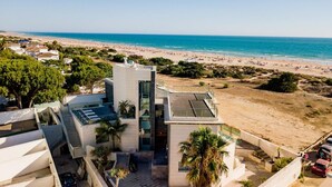 A modern building with a rooftop terrace, adjacent to a beach with visible sand and water. - Hotel Boutique Aroma de Mar (Chiclana de la Frontera)