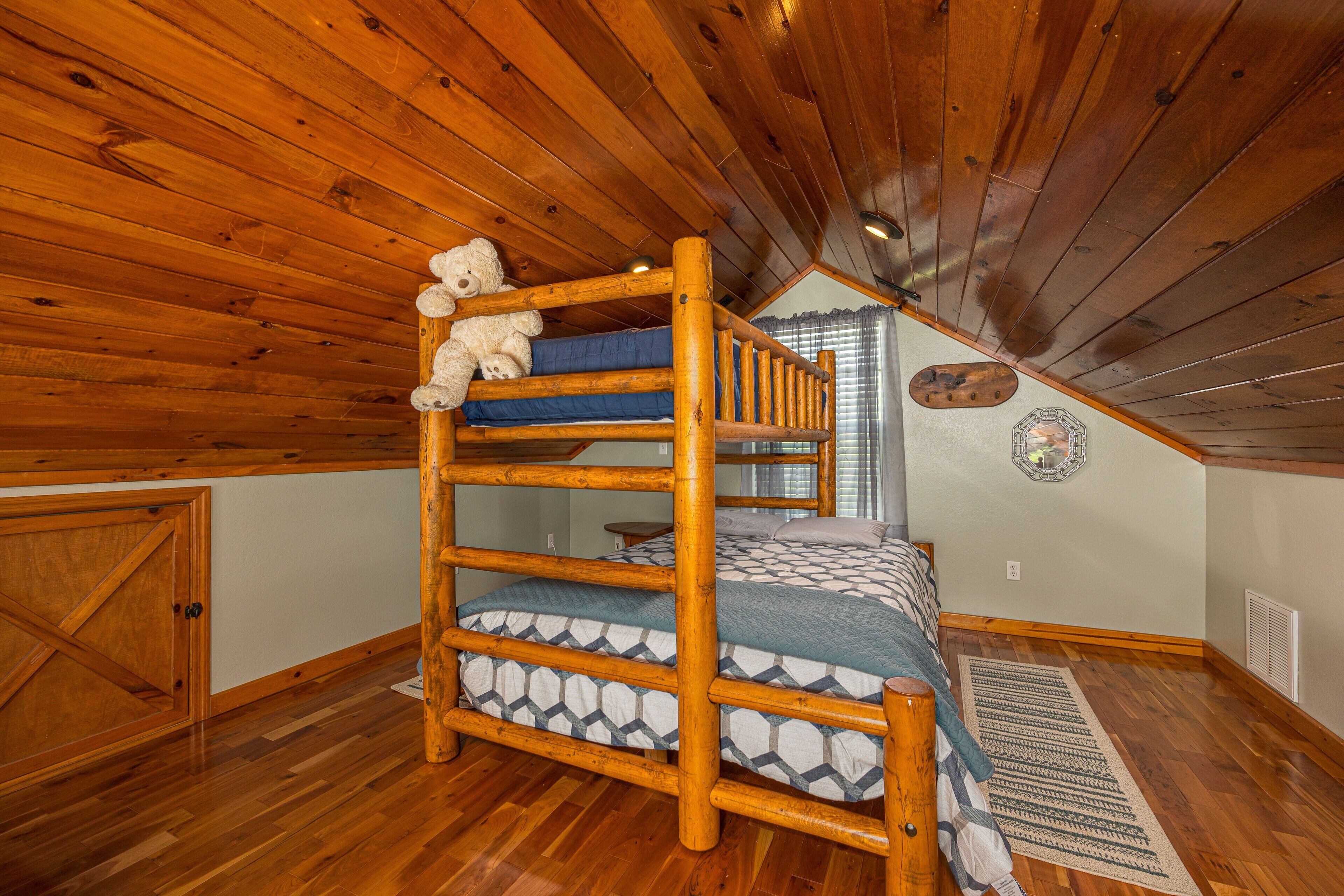 A bunk bed room with wooden beams, a wooden door, and a patterned rug.