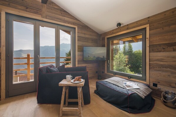 A cozy cabin room with a wooden interior, a sofa, a small table with a croissant, and a TV on the wall. - Chalet Capricorne Alpine Chique Sauna (Riddes)