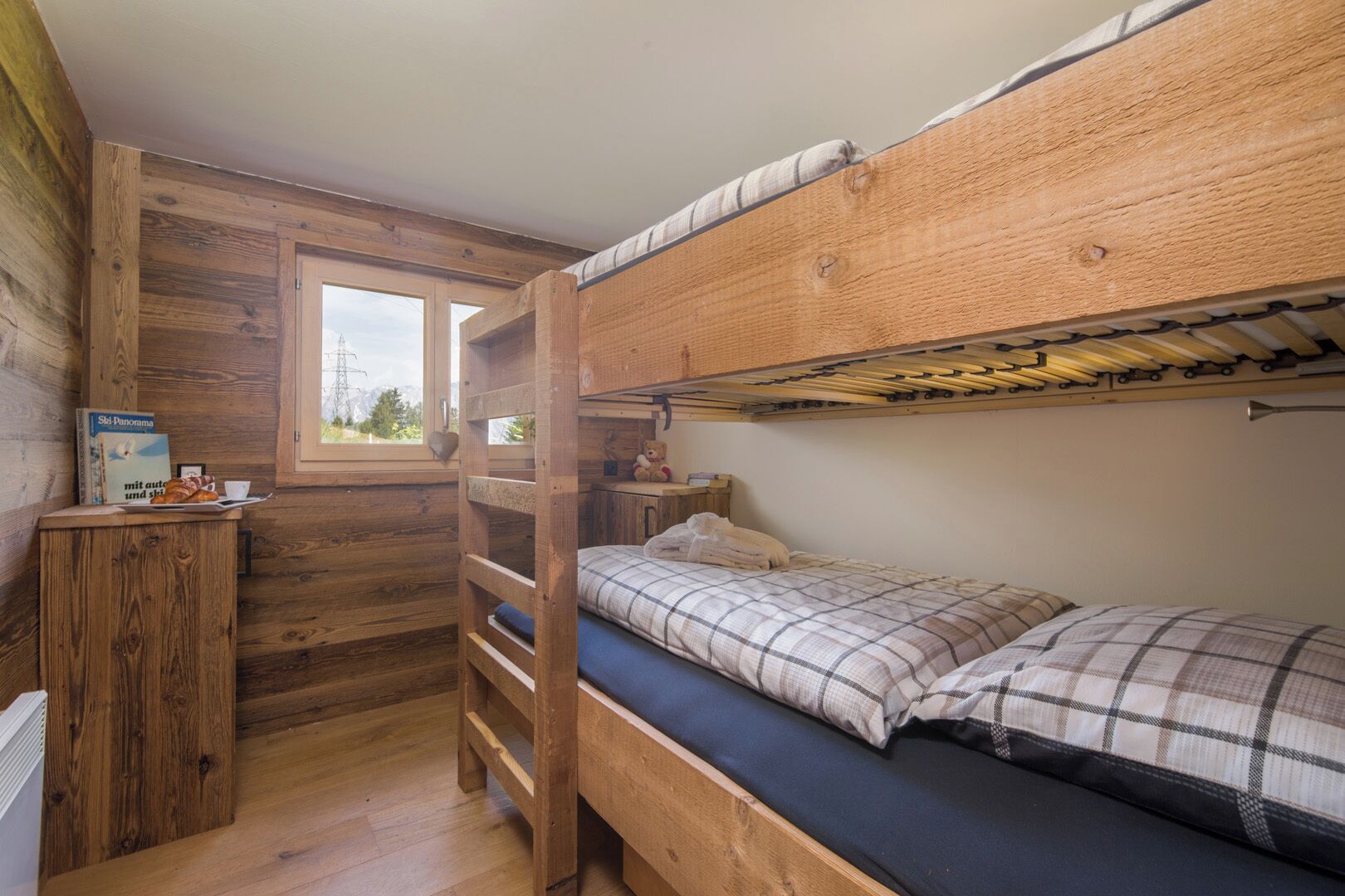 A compact wooden cabin room with bunk beds, a small desk, and a window with a view of the outdoors.