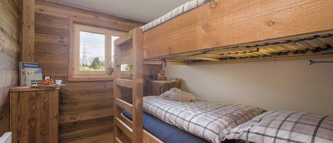 A compact wooden cabin room with bunk beds, a small desk, and a window with a view of the outdoors.