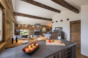 A modern kitchen with wooden beams, a stone fireplace, and a dining area with a large table set for six. - Chalet Capricorne Alpine Chique Sauna (Riddes)
