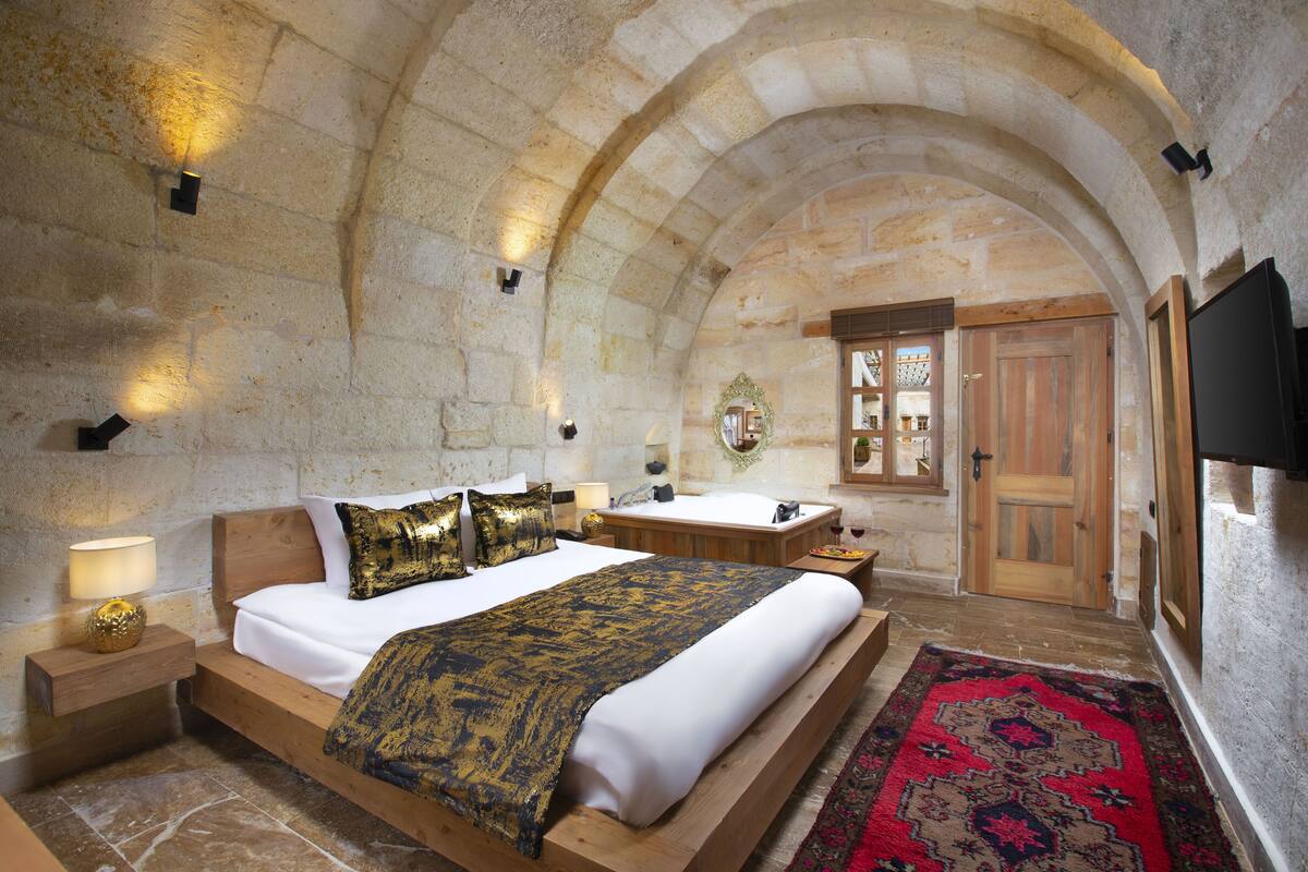 A bedroom with a large bed, wooden headboard, and a red patterned rug.