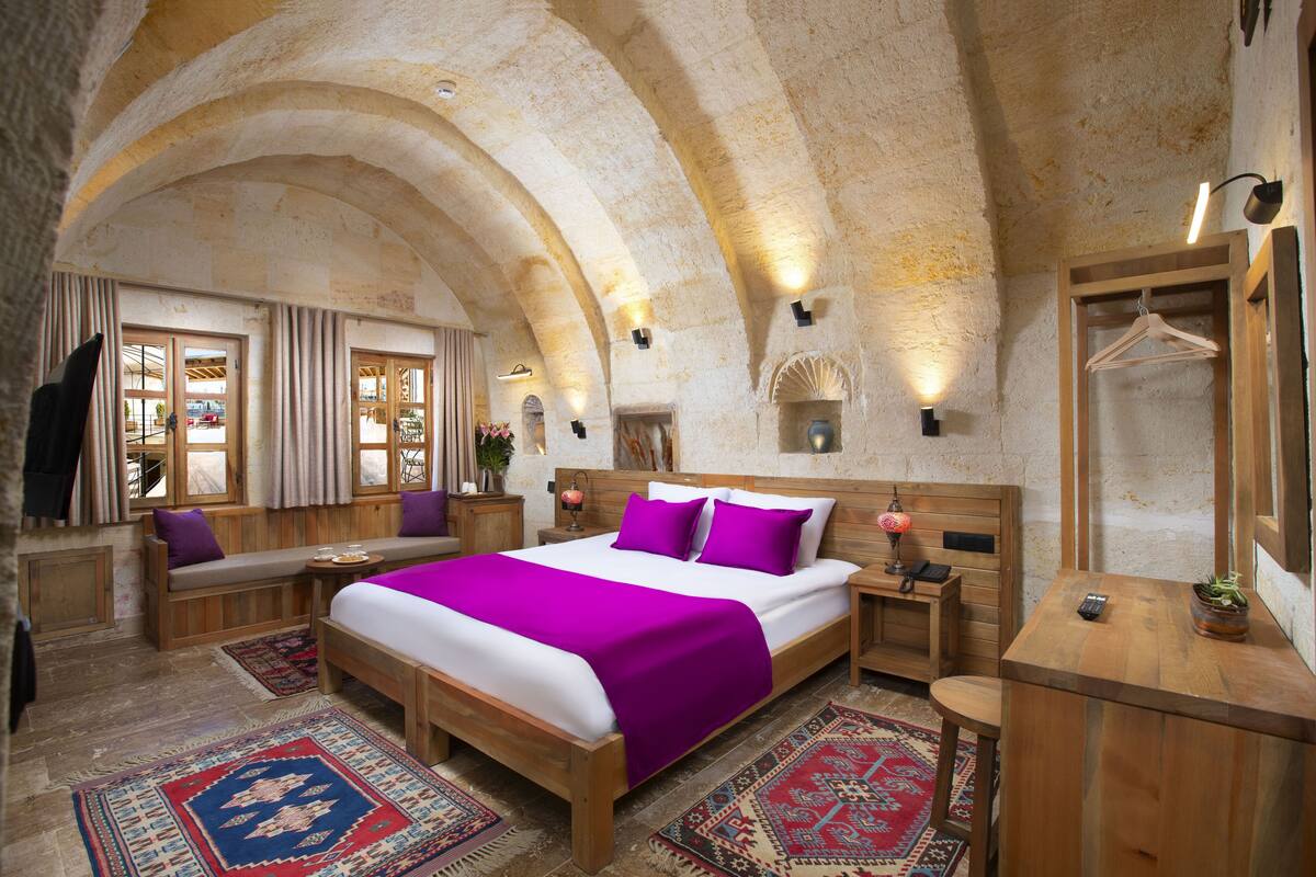 A bedroom with a large bed, wooden headboard, and a bench. There are two bedside tables with lamps and a mirror.