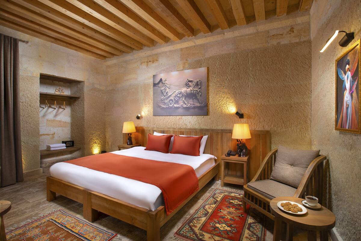 A hotel room with a wooden bed, a sofa, a small table with a plate of cookies, and a painting on the wall.