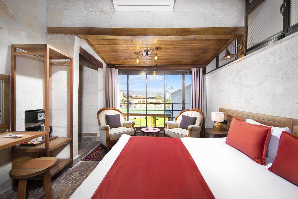 A hotel room with a large bed, two armchairs, a small table, and a desk with a computer.
