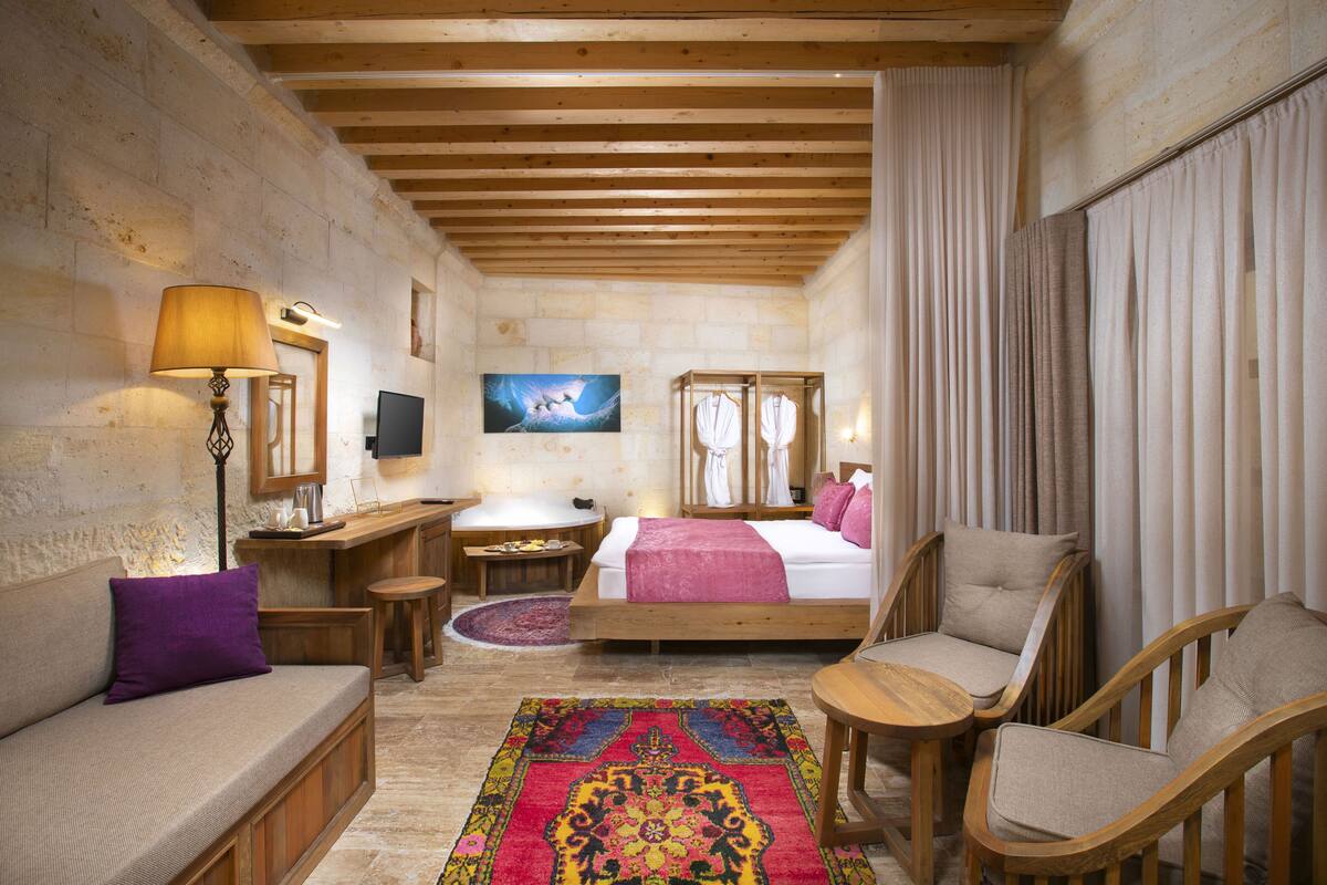 A cozy hotel room with a bed, a sofa, a desk with a lamp, and a television.