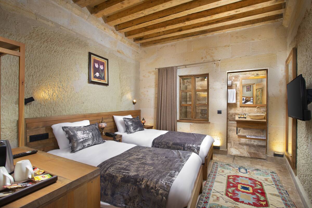 A hotel room with two beds, a wooden ceiling, a large mirror, a television, and a small table with a tray of items.