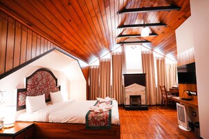 Un dormitorio con techo de madera, una cama con cabecera estampada, una chimenea y un televisor.