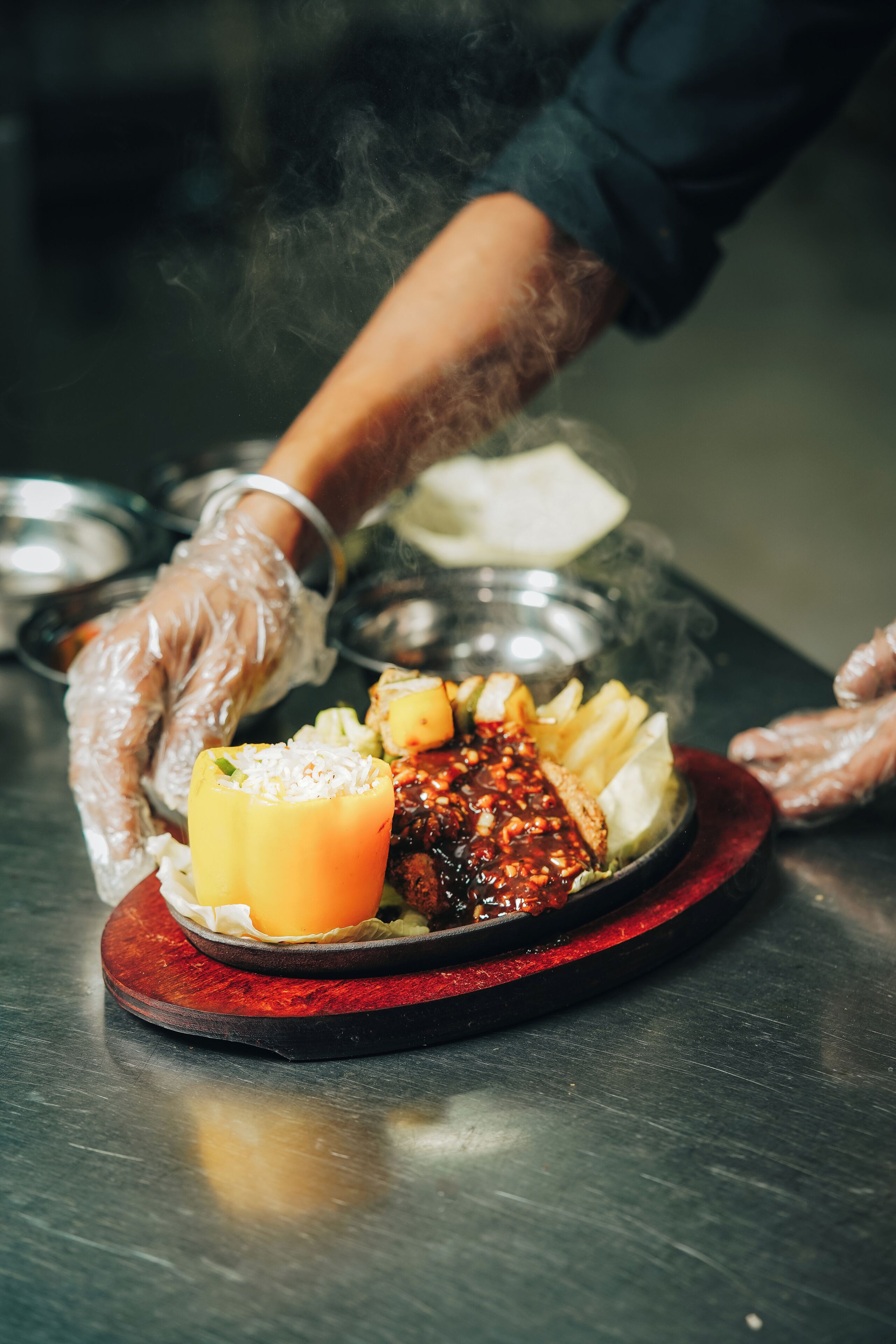 A person wearing gloves preparing food on a stainless steel counter.