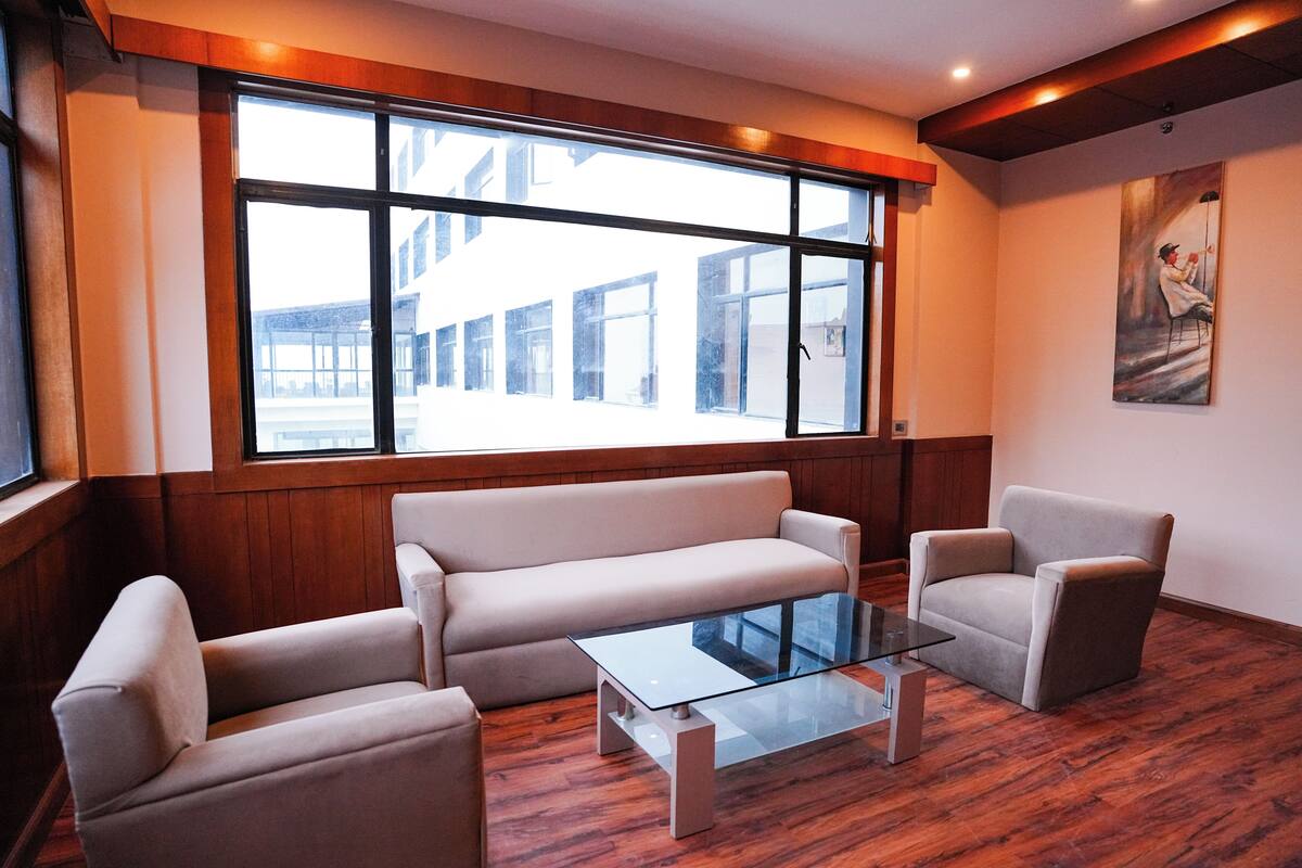 A modern hotel room with a large window, a sofa, a chair, and a glass coffee table.