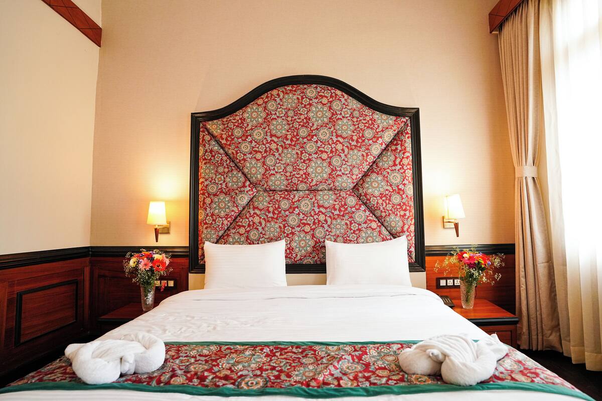 A hotel room with a large bed, two bedside tables with lamps, and floral-patterned headboard.