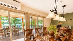 Comedor con una larga mesa de madera dispuesta para una comida, rodeada de sillas, y vistas al exterior a través de grandes puertas de vidrio.