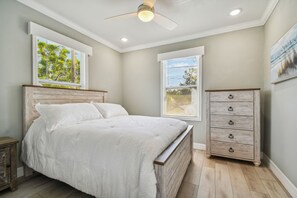 Ein Schlafzimmer mit einem Bett, einem Schminktisch, einem Deckenventilator und zwei Fenstern mit Jalousien.