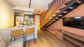 A modern kitchen with a bar area, a staircase, and a TV on the wall.