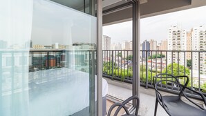 A balcony with a glass partition, a chair, and a view of a cityscape with buildings and greenery. - Charlie For You Moema (São Paulo)