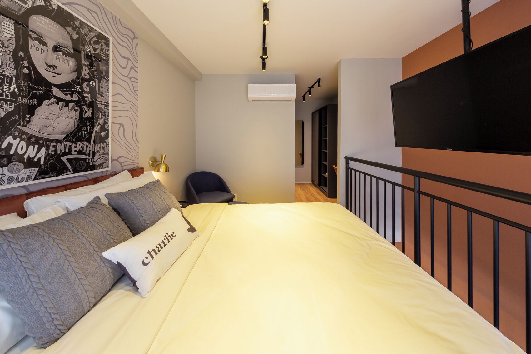 A bedroom with a bed, pillows, a chair, a TV, and an air conditioning unit.