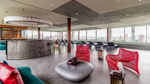 A spacious lobby with a modern design, featuring a curved reception desk, comfortable seating areas, and large windows offering a city view. - Charlie For You Moema (São Paulo)