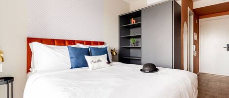 A modern hotel room with a large bed, a wardrobe, and a small table.