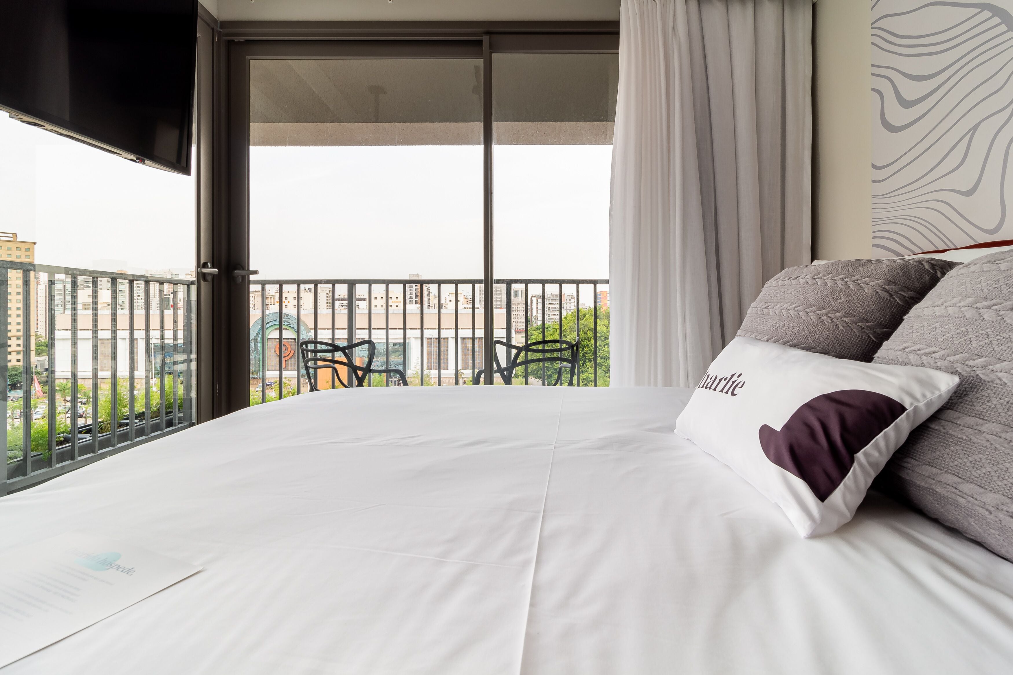 A hotel room with a large bed, a balcony with a view of the city, and a TV mounted on the wall.