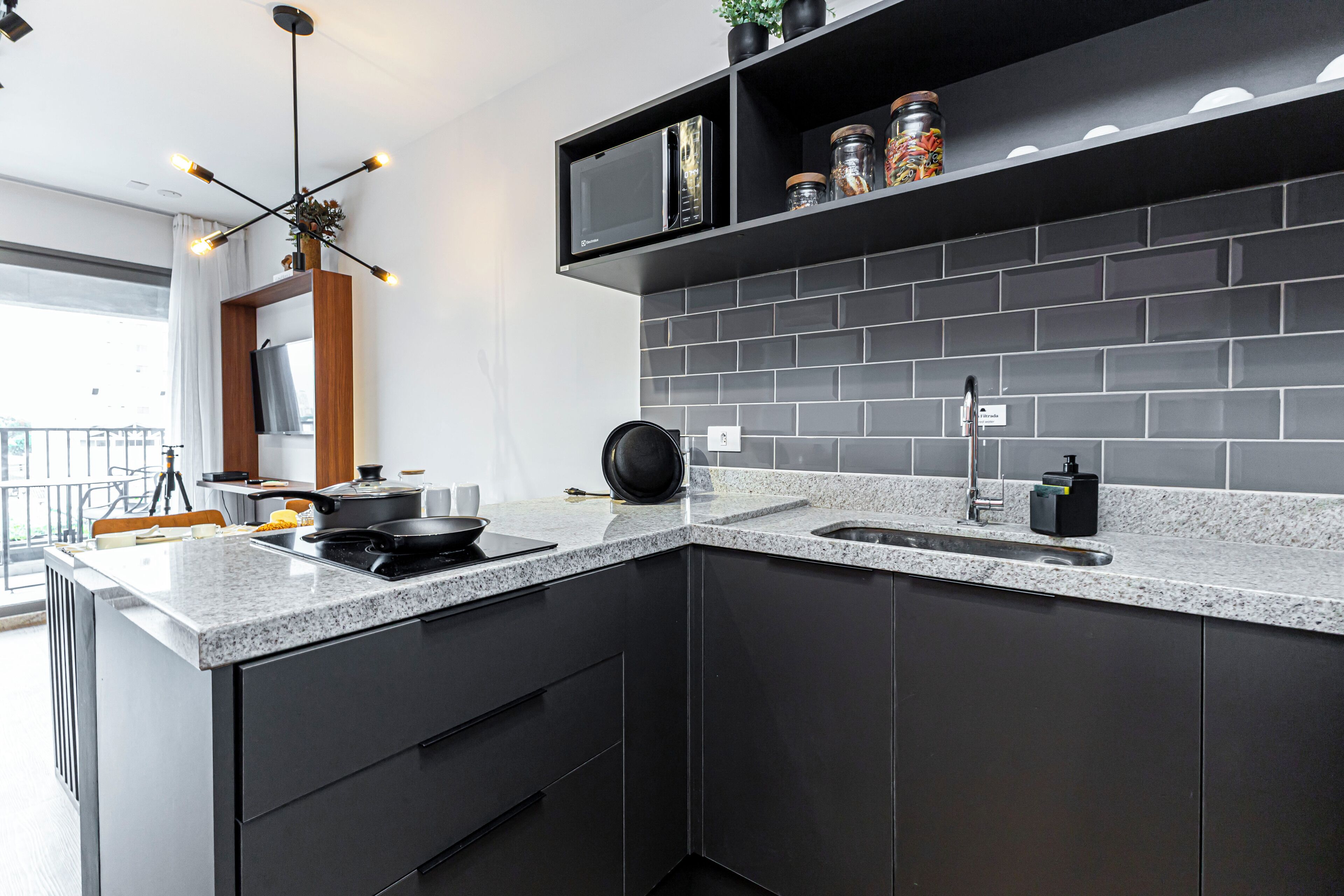 Een moderne keuken met donkere kastjes, een granieten aanrechtblad, een ingebouwde magnetron en een zwarte pan op het fornuis.