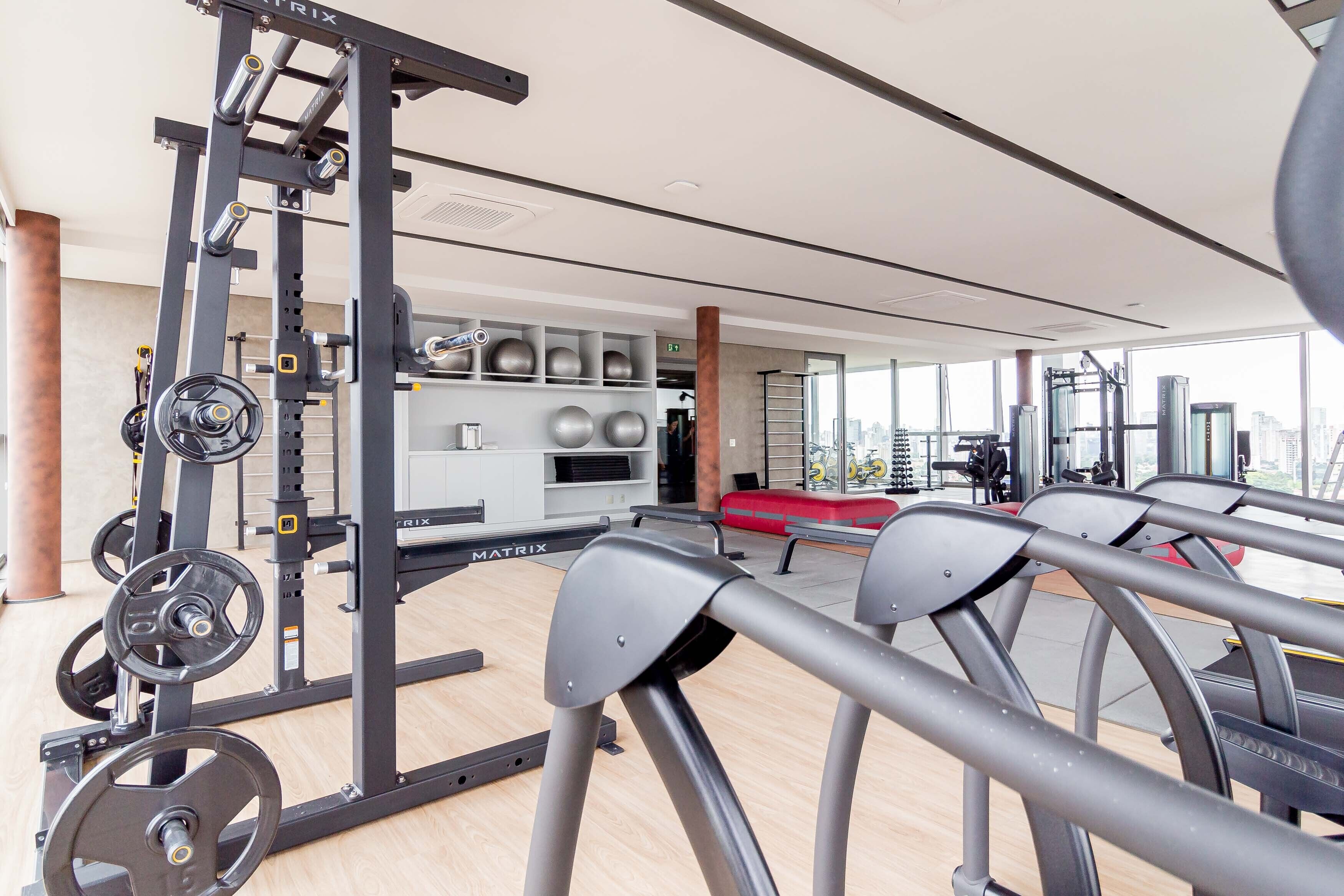 A modern gym with weightlifting equipment, treadmills, and a large window offering a city view.