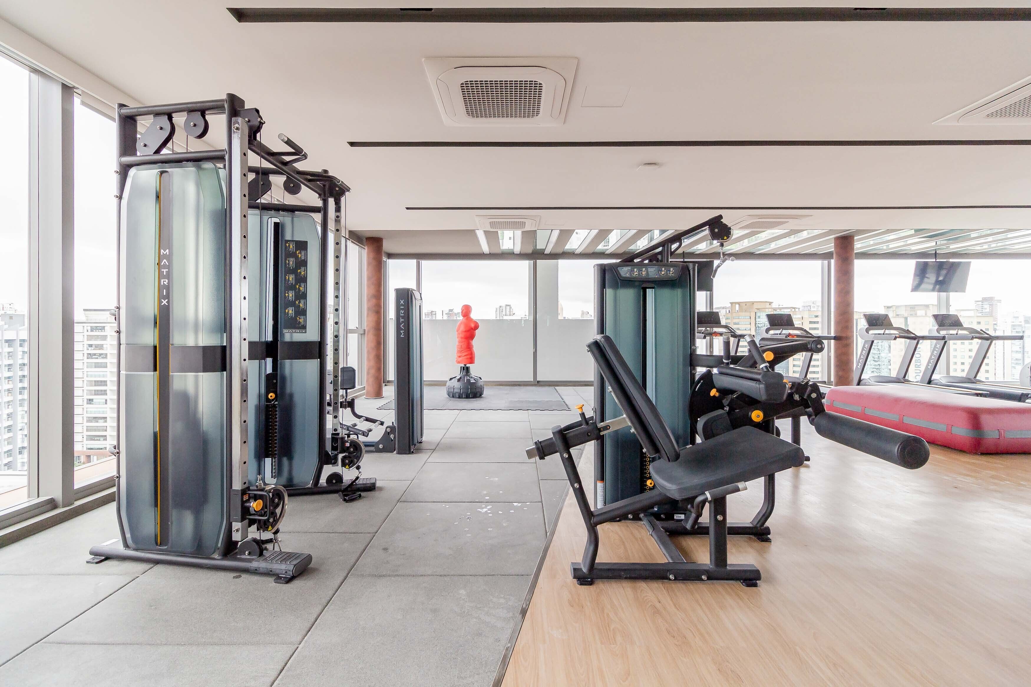 A modern gym with various exercise equipment, large windows, and a city view.