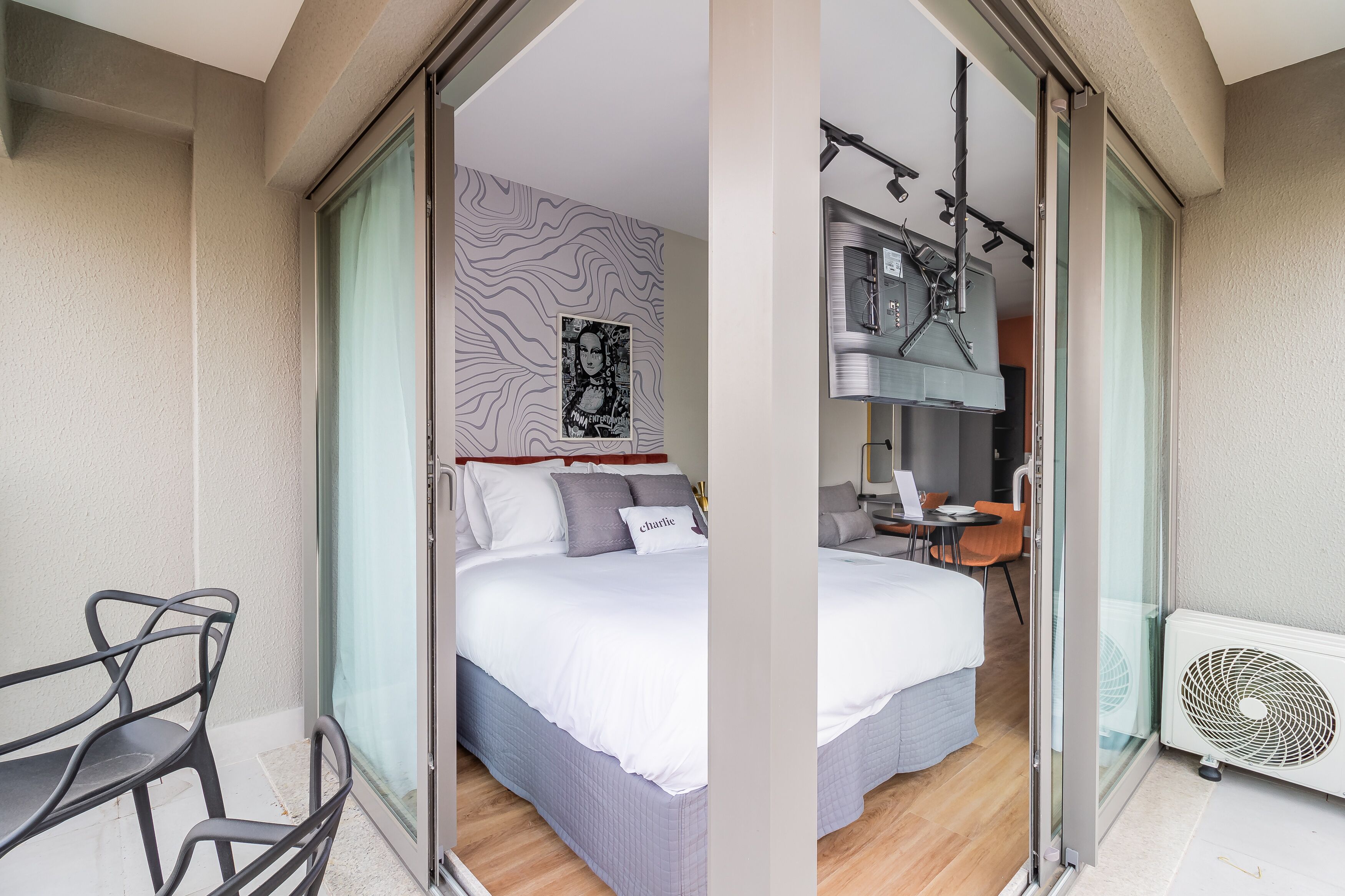 A hotel room with a bed, a desk, a chair, a window with curtains, a wall with a patterned design, and a ceiling fan.