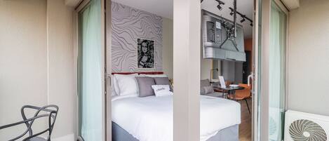A hotel room with a bed, a desk, a chair, a window with curtains, a wall with a patterned design, and a ceiling fan.