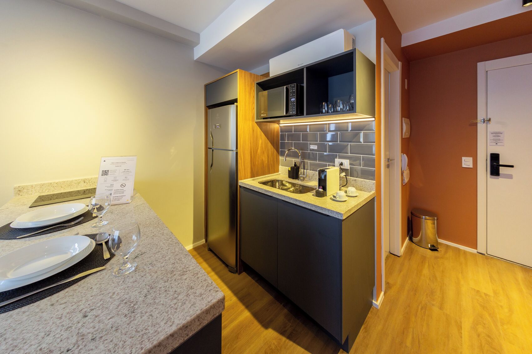A compact kitchen with a built-in microwave, a sink, and a refrigerator. There is a small countertop with a coffee maker and cups.