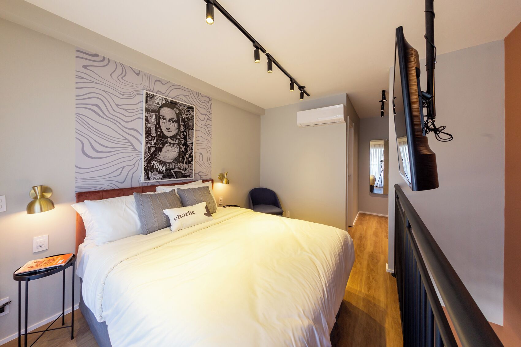 Ein modernes Schlafzimmer mit einem großen Bett, einer Wandklimaanlage, einem Schreibtisch mit Lampe und einem Poster an der Wand.