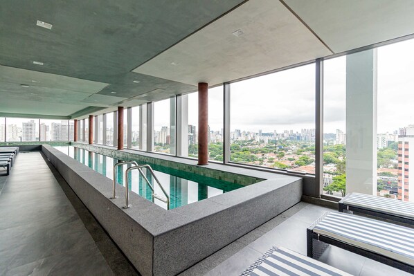 Una piscina interior moderna con vistas a la ciudad, ventanas amplias y un diseño minimalista.
