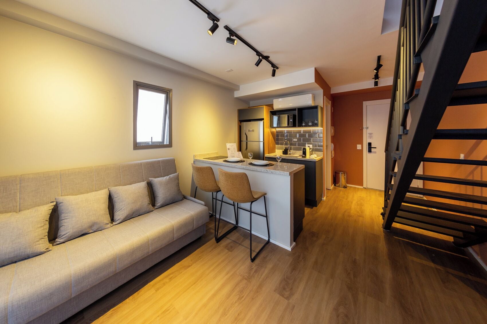 A compact living space with a sofa, a small kitchen area, and a staircase.