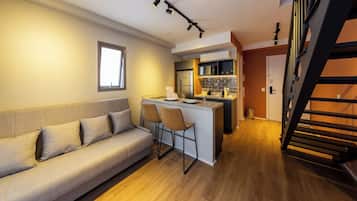 A compact living space with a sofa, a small kitchen area, and a staircase.