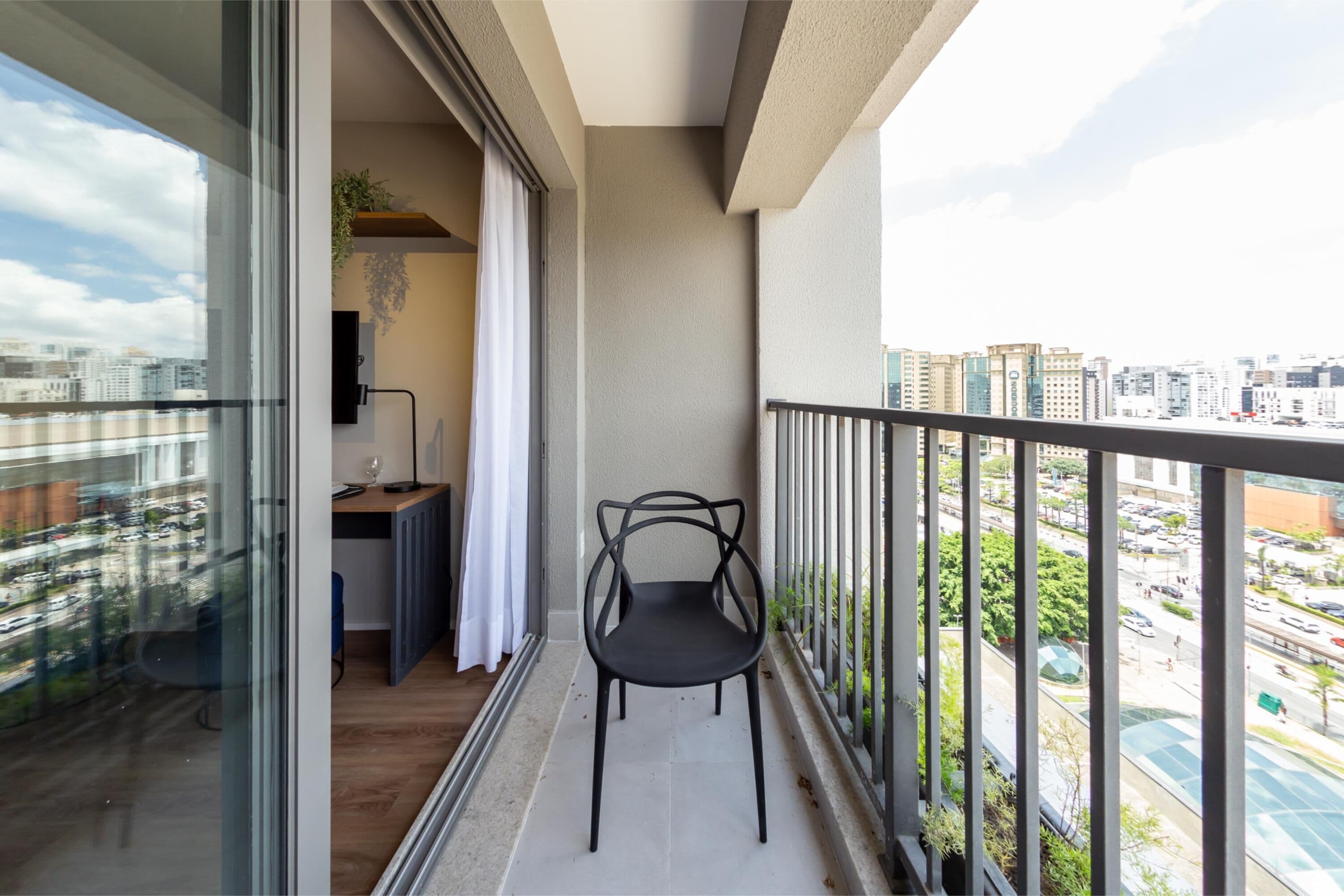 A balcony with a chair, a desk, and a view of a cityscape.