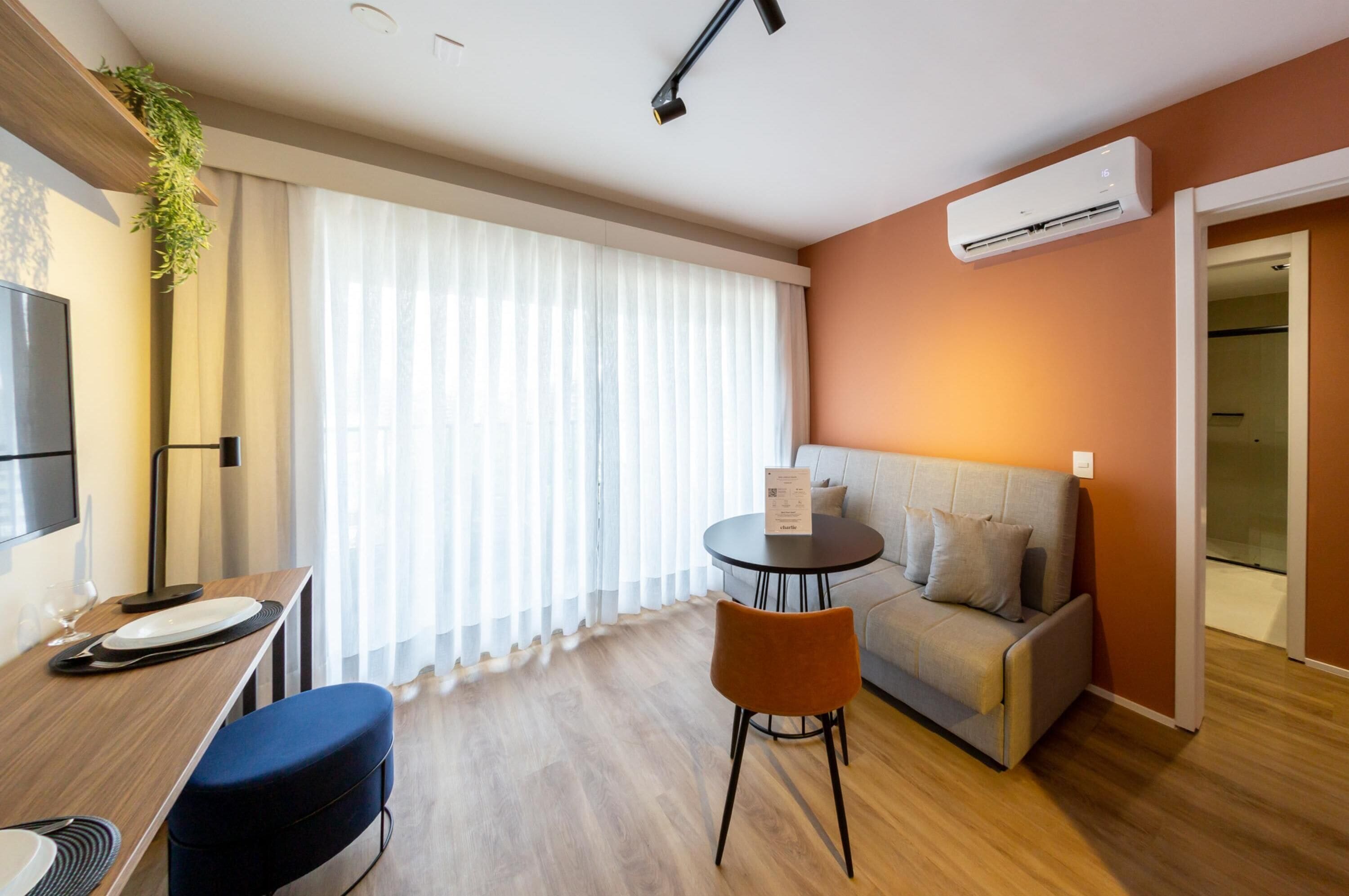 A modern living room with a sofa, a dining table with chairs, a TV, and an air conditioning unit.