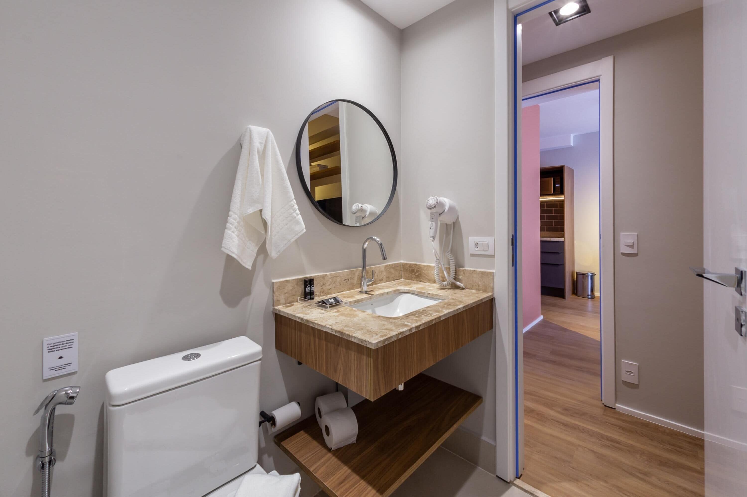 A modern bathroom with a wooden vanity, a round mirror, a toilet, and a shower.