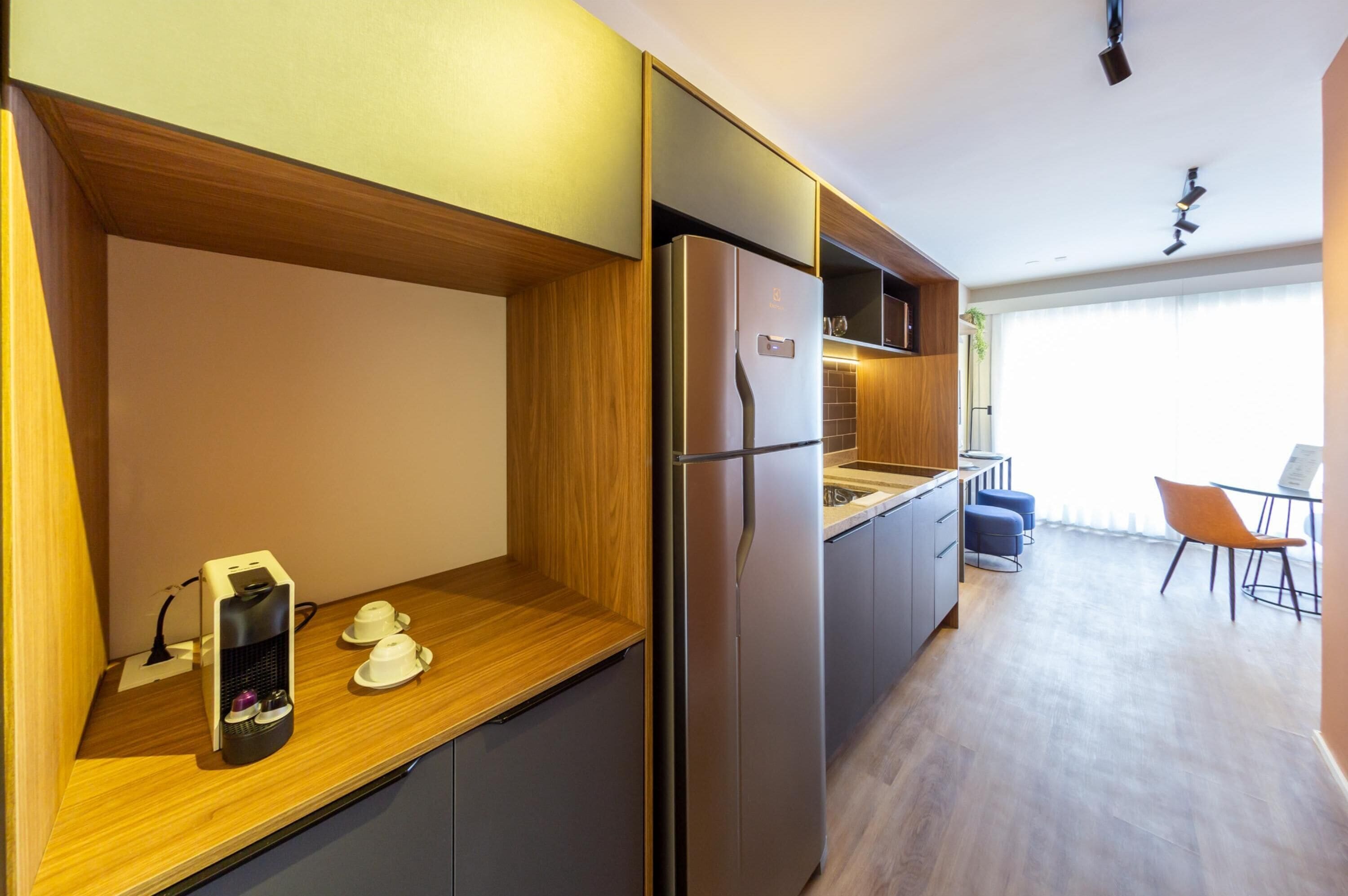 A compact kitchen with a built-in refrigerator, wooden countertop, and a small seating area with a chair and table.