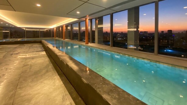 A modern indoor swimming pool with large windows offering city views. - Charlie For You Moema (São Paulo)