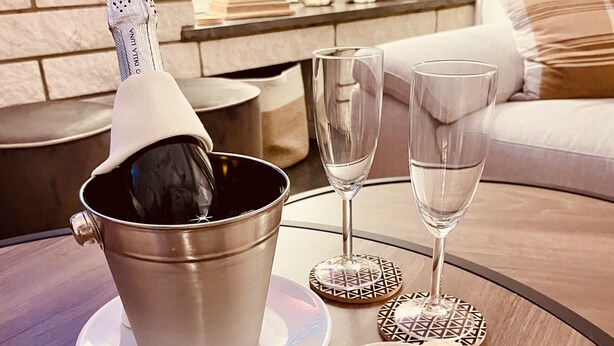 Een tafel met een champagnefles in een emmer, twee lege wijnglazen en twee borden met koekjes.