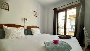 Een hotelkamer met een groot bed, een raam met gordijnen, een stoel en een kleine tafel met een bloem.
