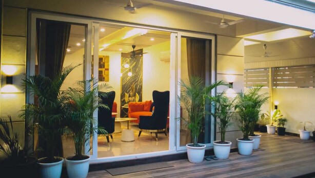 A modern hotel lobby with a glass entrance, indoor plants, and a seating area with a sofa and chairs.