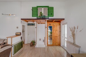 Ein großzügiger Wohnbereich mit Holzboden, einem grünen Fenster, einer Heizung und einer Holztür, die in einen anderen Raum führt.