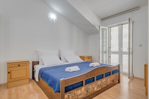 A bedroom with a wooden bed, white pillows, a blue bedspread, and a wooden nightstand. - Spacious apartment Zvone with 3 balconies and parking (Split)